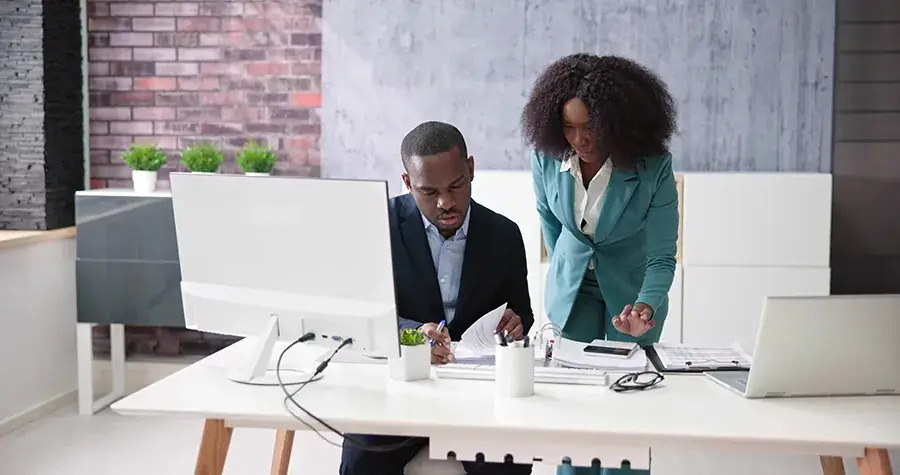 1. Two individuals collaborating at a desk in a professional office environment, focused on their tasks.