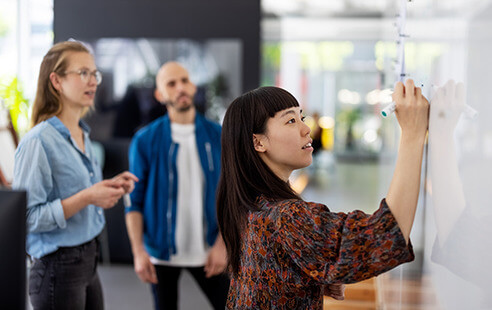 A diverse group of individuals gathered around a whiteboard, engaged in discussion and collaboration.